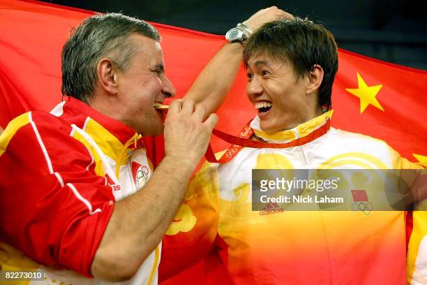Zhong Man of China smiles as his coach Christian Bauer bites his gold medal for the men's fencing individual sabre held at the Fencing Hall of...