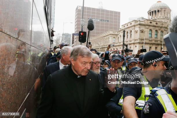Cardinal George Pell walks with a heavy Police guard from the Melbourne Magistrates' Court as he waves to supporters on July 26, 2017 in Melbourne,...