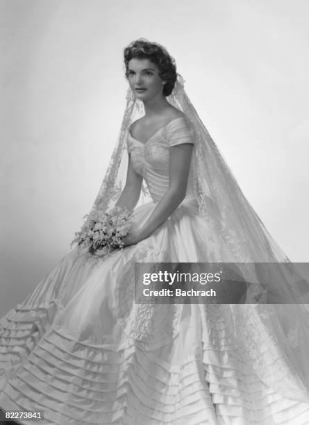 Bridal portrait of Jacqueline Lee Bouvier shows her in an Anne Lowe-designed wedding dress, a bouquet of flowers in her hands, New York, New York,...