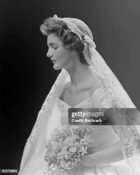 Bridal portrait of Jacqueline Lee Bouvier shows her in an Anne Lowe-designed wedding dress, a bouquet of flowers in her hands, New York, New York,...