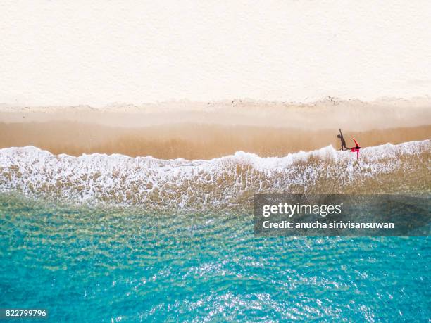 people wearing red shirts walking footprints on the beach white with blue sea waves , aerial view . - on top of photos et images de collection