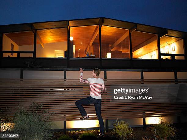 woman climbing fence in front of house, night - entrometido fotografías e imágenes de stock