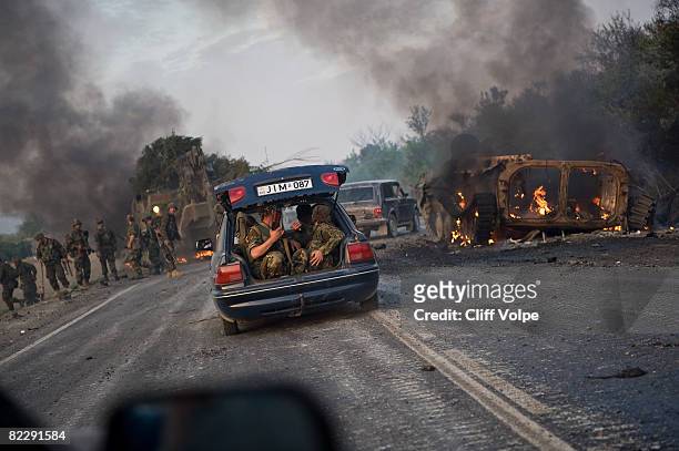 Georgian troops ride in a civilian vehicle as a Georgian Armoured Personel Carrier lies wrecked on the road between Gori and Tibilisi, on August 11,...