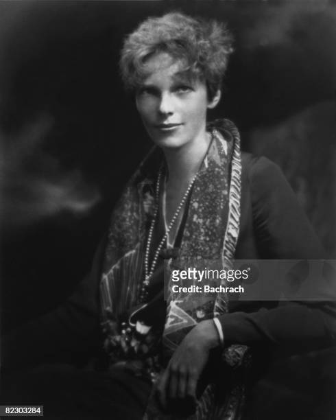 Portrait of American aviator Amelia Earhart as she poses in an armchair, a print scarf over her shoulders, early 1930s.
