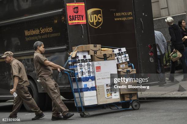 United Parcel Service Inc. Delivery driver pulls a dolly of packages to be delivered past a truck on a street in New York, U.S, on Monday, July 24,...