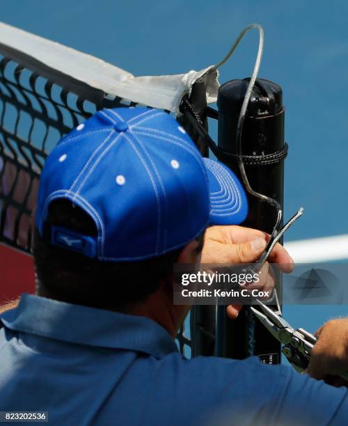 Court attendant repairs the broken cable that holds up the net in the match between Quentin Halys of France and Gilles Muller of Luxembourg during...