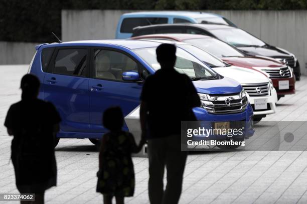 Silhouetted visitors walk towards Nissan Motor Co. Vehicles, including a Dayz Highway Star vehicle, front, on display outside the company's showroom...