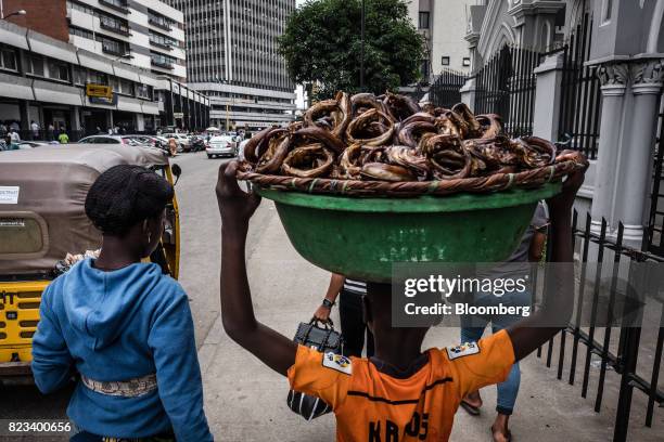 Street seller carries a basket of fish along a sidewalk in Lagos, Nigeria, on Wednesday, July 26, 2017. Nigeria's economy, which in 2016 suffered its...