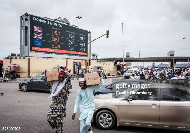 Pedestrians carry boxes of goods across a busy road near a giant advertising screen showing US dollar, British pound and euro foreign currency...