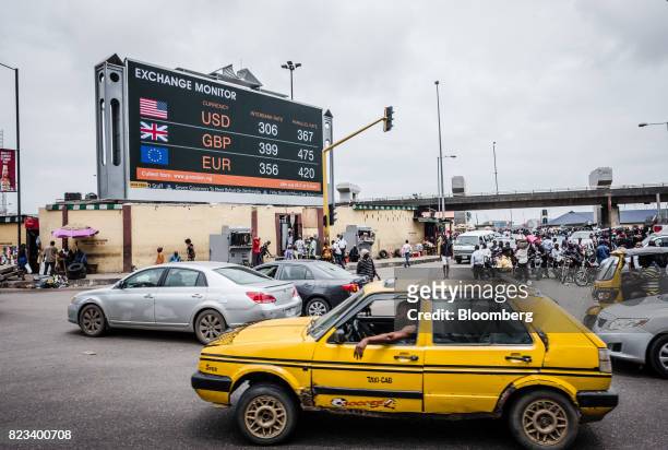 Taxi cab passes a giant advertising screen showing US dollar, British pound and euro foreign currency exchange rates on a busy city road in Lagos,...