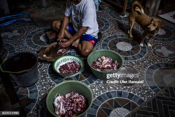 Man cuts up dog meat as a dog watches during the slaughter process at a dog meat butchery house on July 25, 2017 in Yogyakarta, Indonesia....
