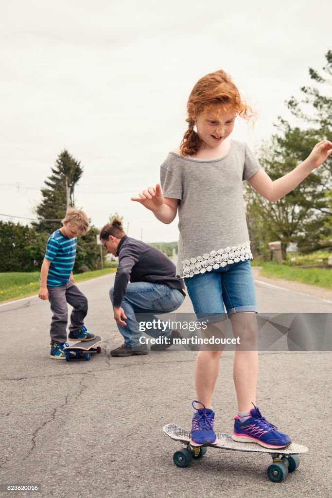 Papá enseña a los niños a monopatín en la calle rural