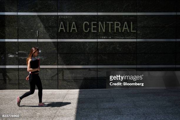 Pedestrian walks past signage for the AIA Central building, which houses the headquarters of AIA Group Ltd., in Hong Kong, China, on Friday, July 28,...