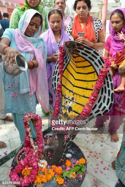 This photo taken on July 27, 2017 shows Indian Hindu devotees pouring milk over a statue of a cobra snake during the Nag Panchami festival at a...