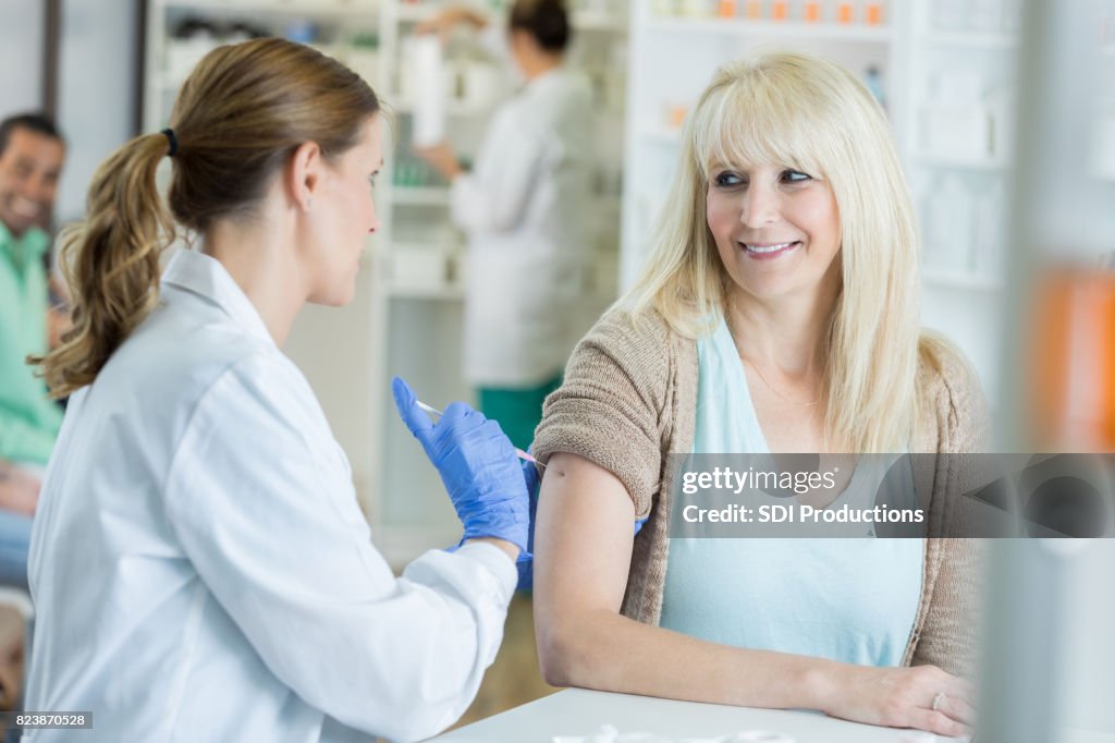 Pharmacist pushes needle into arm of smiling patient during flu shot