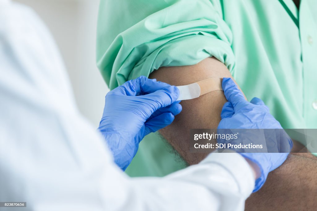 Closeup of unrecognizable pharmacist placing bandaid on customer's arm