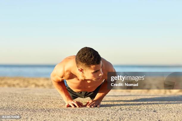 joven atleta masculino haciendo flexiones de diamante en la playa - flexiones fotografías e imágenes de stock
