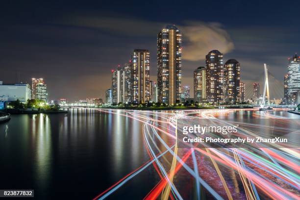 tokyo cityscape of tsukishima skyscrapers at night with houseboat light trails over sumida river,tokyo japan. - tsukishima tokyo stock pictures, royalty-free photos & images