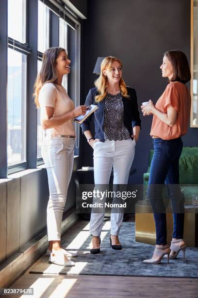 businesswomen discussing by window in office - three people standing stock pictures, royalty-free photos & images