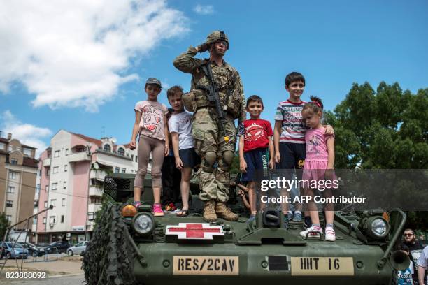 Soldier salutes while the US national anthem next to Macedonian children on a US army vehicle during a presentation of US vehicles and weapons in...