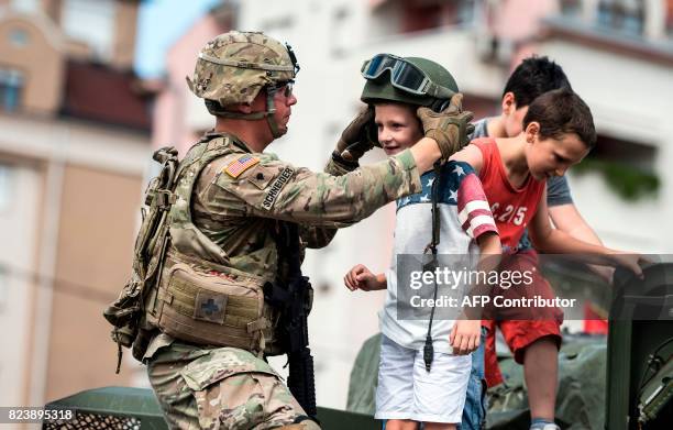 Soldier puts a helmet on a child as they stand on a US army vehicle during a presentation of US vehicles and weapons in Kumanovo on July 28, 2017....