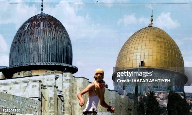 Palestinian protesters stands in front of a mural covered in an image of the Dome of the Rock during clashes between demonstrators and Israeli...