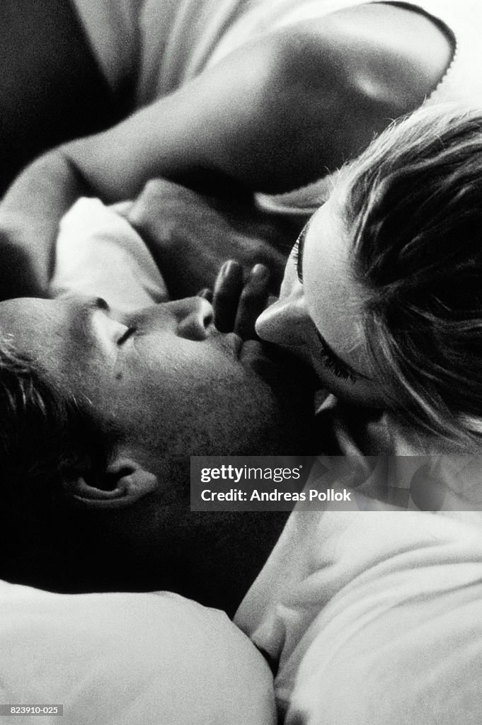 Young couple kissing in bed, close-up (B&W)