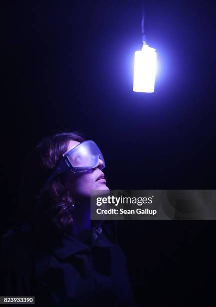 Visitor wearing milky goggles and devices strapped to her body that emit light in different colors and have haptic engines pauses as she walks...