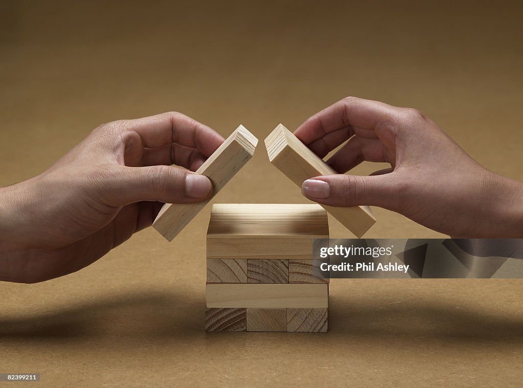 Hands forming a house from wooden blocks