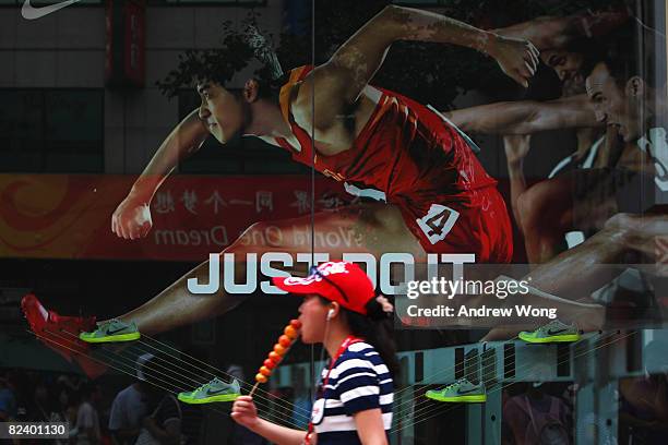 Chinese woman eats snack as she walks past an advertisement featuring defending Olympic 110 metres hurdles champion Liu Xiang on August 18, 2008 in...