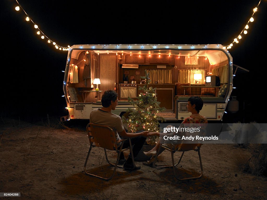 Man and woman sitting by tree next to home