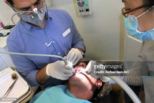 dentist and dental assistance treating teeth of a patient - surgical loupes stock pictures, royalty-free photos & images