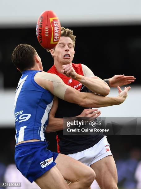 Mitch Hannan of the Demons handballs whilst being tackled by Aaron Mullett of the Kangaroos during the round 19 AFL match between the North Melbourne...