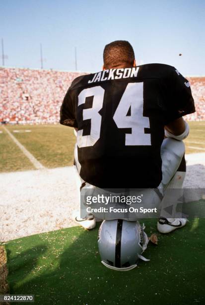 Bo Jackson of the Los Angeles Raiders sitting on his helmet looks on from the sidelines during an NFL Football game circa 1989 at the Los Angeles...