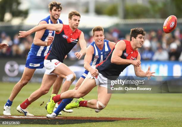 Christian Petracca of the Demons handballs whilst being tackled by Andrew Swallow of the Kangaroos during the round 19 AFL match between the North...