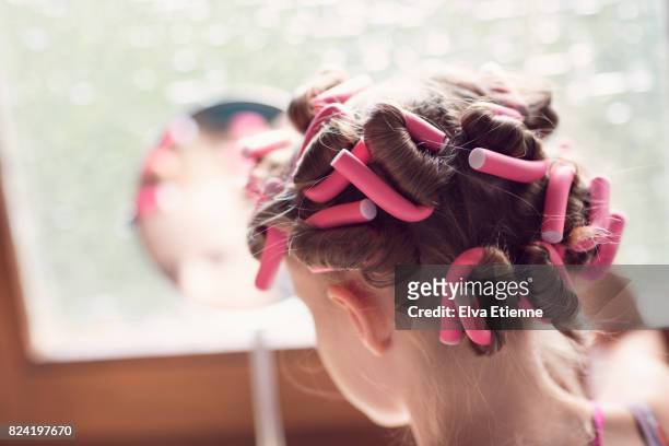 girl (10-11) in pink hair rollers, looking in a mirror - hair curlers stock-fotos und bilder