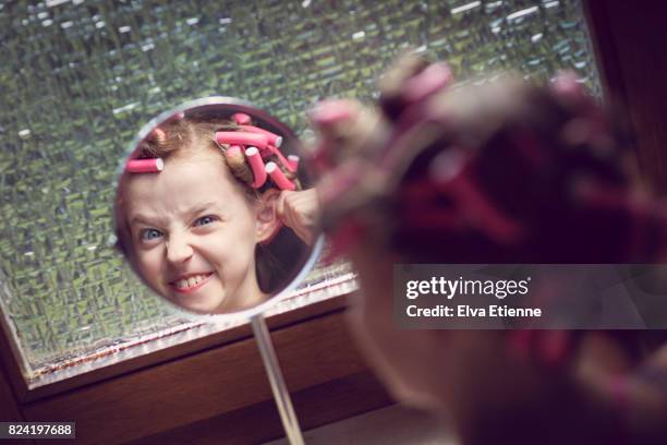 girl in hair rollers, looking in mirror and pulling silly face - child pulling hair stock pictures, royalty-free photos & images