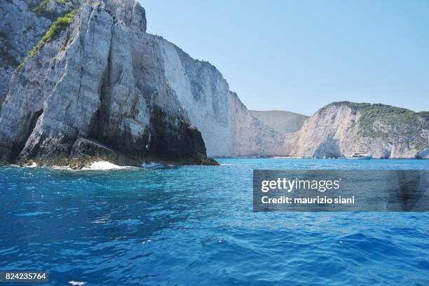 caves by blue sea against sky and famous navagio shipwreck beach. zakynthos, greece - agios georgios church stock-fotos und bilder