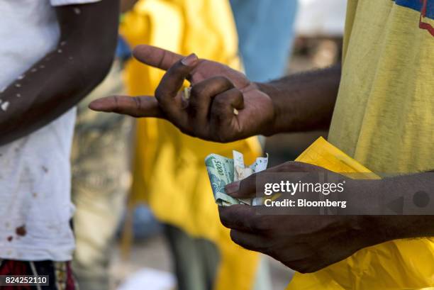 Customer holds West African CFA franc currency banknotes at the Soumbedioune fish market in Dakar, Senegal, on Friday, July 28, 2017....