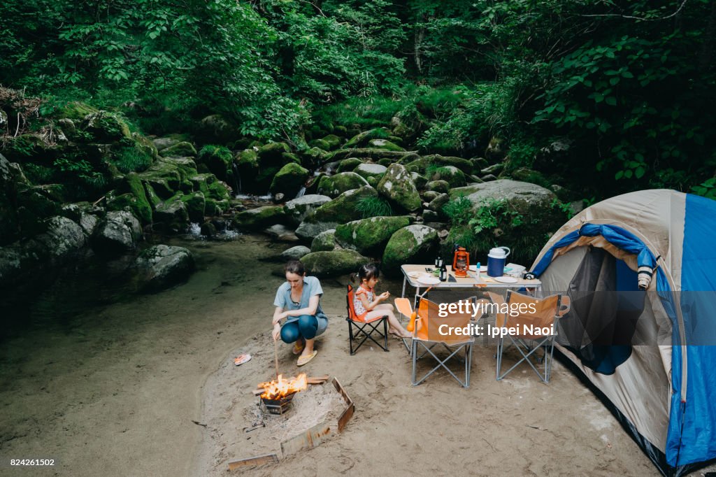 Family camping by stream in forest, Japan