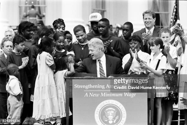 President Bill Clinton is surrounded by children while signing a legislation to raise the minimum wage during a ceremony on the South Lawn of the...