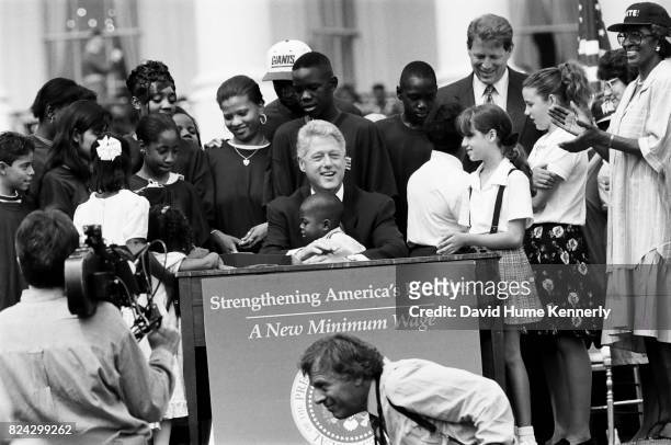 President Bill Clinton, surrounded by children, signs legislation to raise the minimum wage during a ceremony on the South Lawn of the White House,...