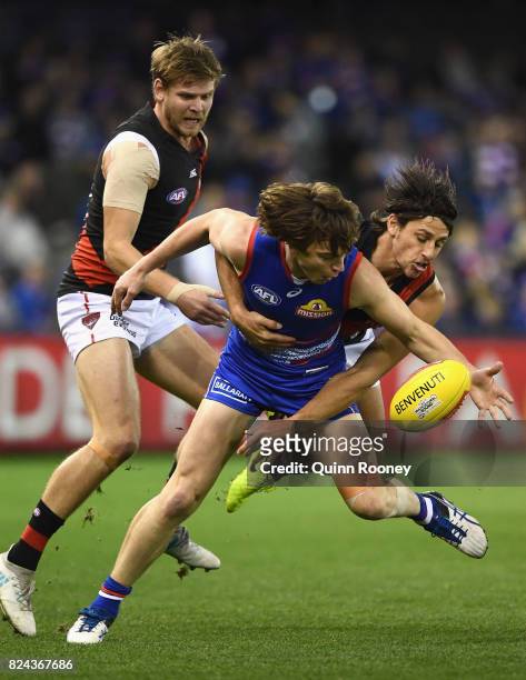 Liam Picken of the Bulldogs is tackled by Michael Hurley and Mark Baguley of the Bombers during the round 19 AFL match between the Western Bulldogs...