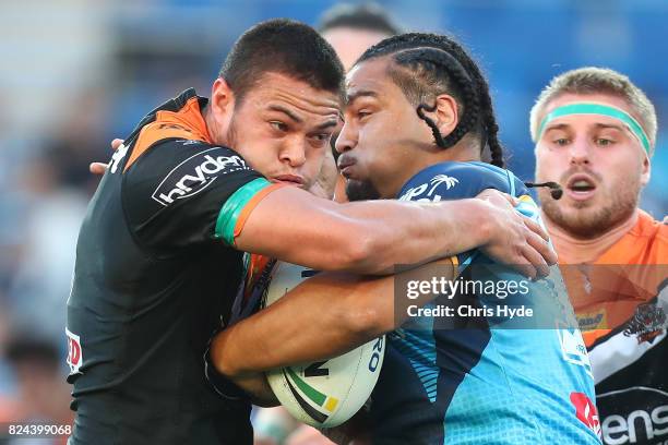 Leivaha Pulu of the Titans is tackled by Tuimoala Lolohea of the Tigers during the round 21 NRL match between the Gold Coast Titans and the Wests...