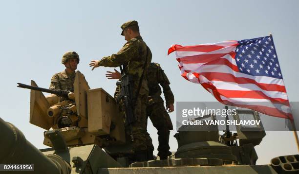 Soldier and a German soldier talk while standing on an Abrams Battle Tank bearing the US flag prior to the opening ceremony of the joint...