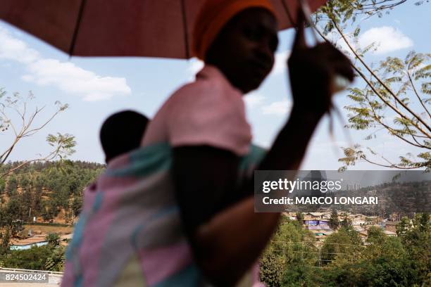 Woman carries her baby on her back as houses and buildings in the city of Kigali are seen in the background, on July 30, 2017. The presidential...