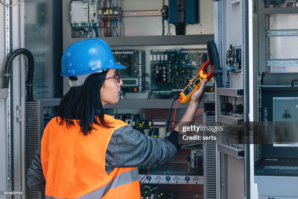 Young female maintenance engineer testing voltage with digital multimeter
