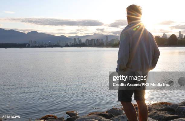 man pauses on coastal rocks to look out at city, sunrise - look back stockfoto's en -beelden