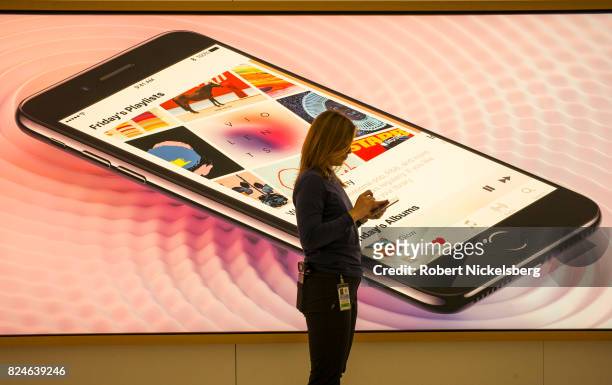 An Apple employee uses her iPhone while standing in front of an advertisement at the Apple retail store July 22, 2017 at the World Trade Center in...
