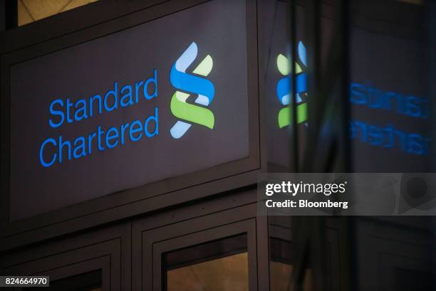 The logo for Standard Chartered Plc is displayed atop an entrance to the Standard Chartered Bank building in Hong Kong, China, on Sunday, July 30,...